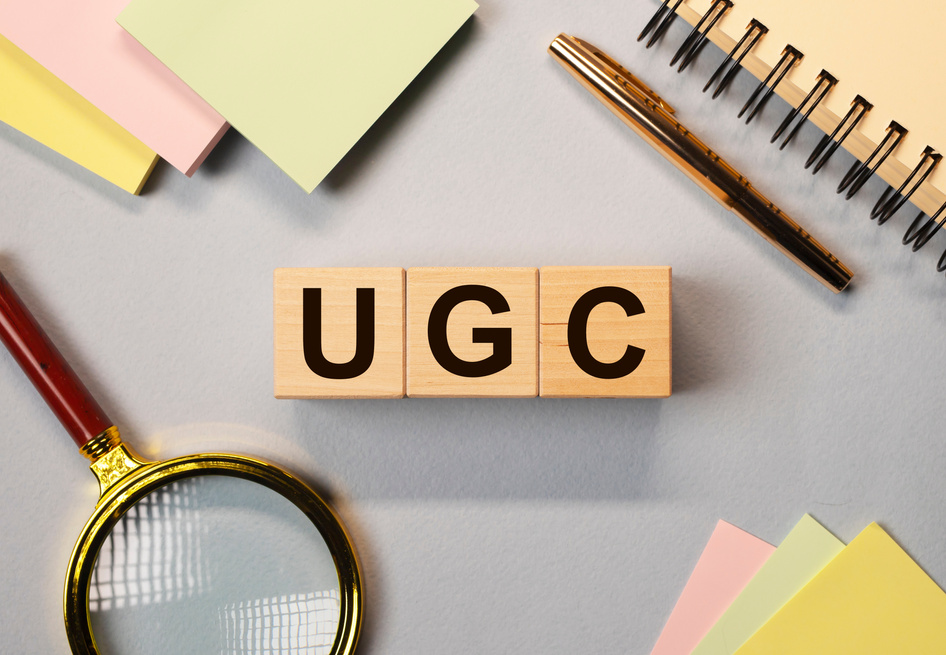 UGC Acronym Text with Loupe and Notepads on Background